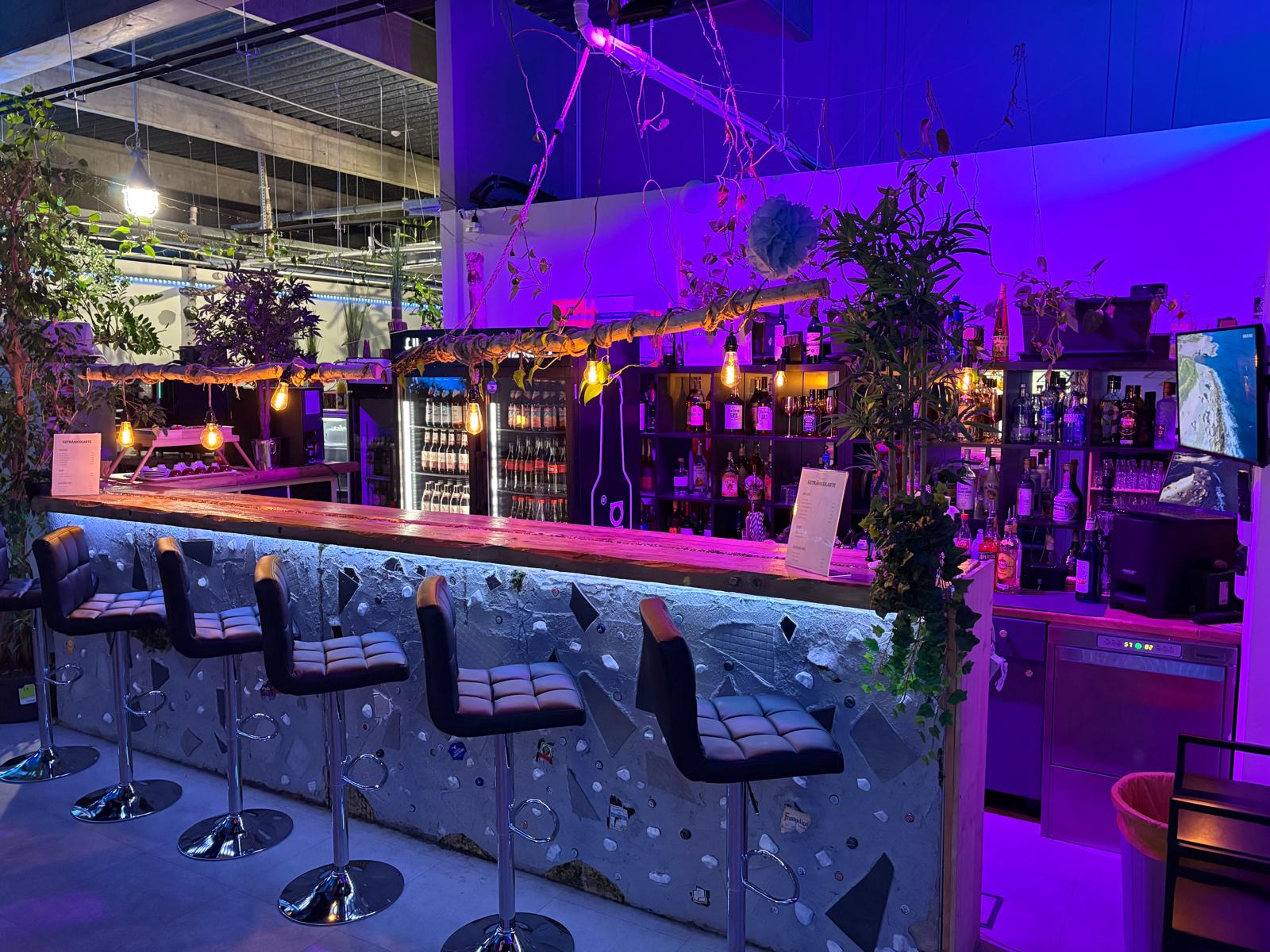 Eventbar mit lila Beleuchtung, Barhockern und atmosphärischer Bepflanzung